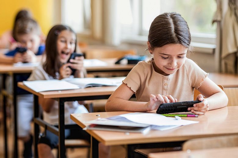 1329102134 Kinder sitzen an Schulbänken und benutzen ihre Smartphones.