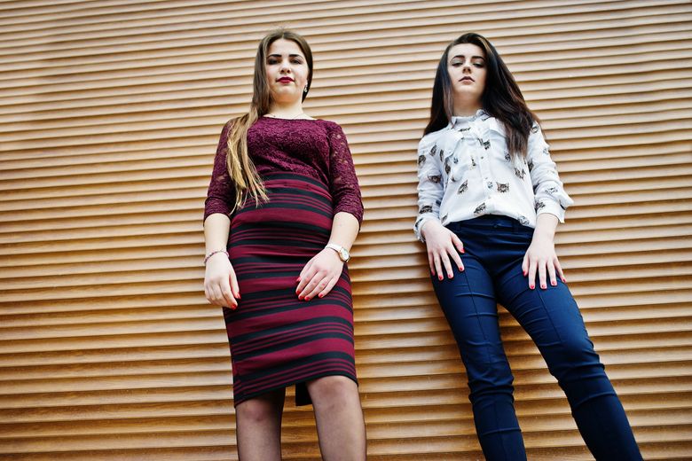 Two young teenages girl posed against orange shutter. Plump girl vs thin. Zwei junge Frauen blicken selbstbewusst in die Kamera. Foto: istock/ASphotowed