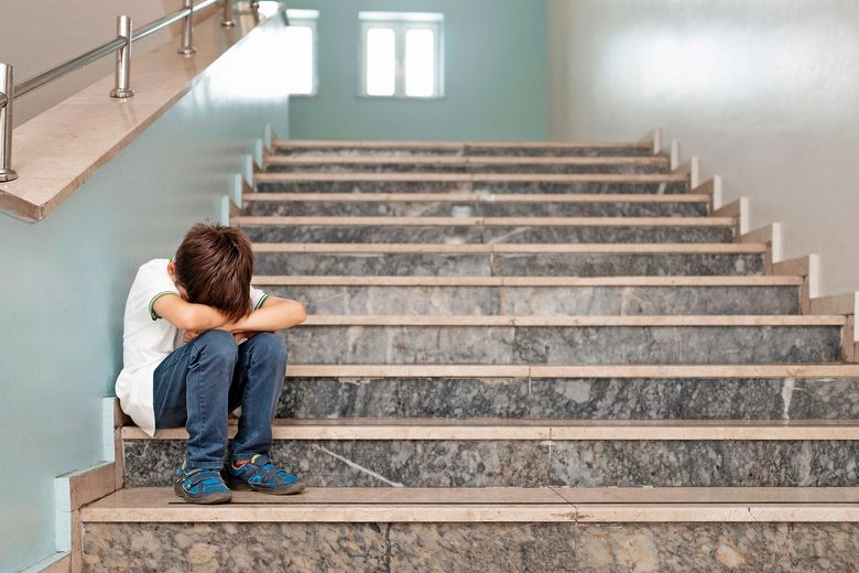 1440456021 Ein Kind sitzt auf einer Treppe und verbirgt sein Gesicht hinter seinen Knien.