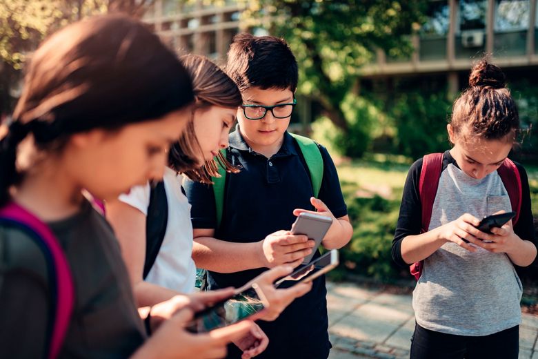 Schülerinnen und Schüler stehen nebeneinander und schauen in ihre Handys.