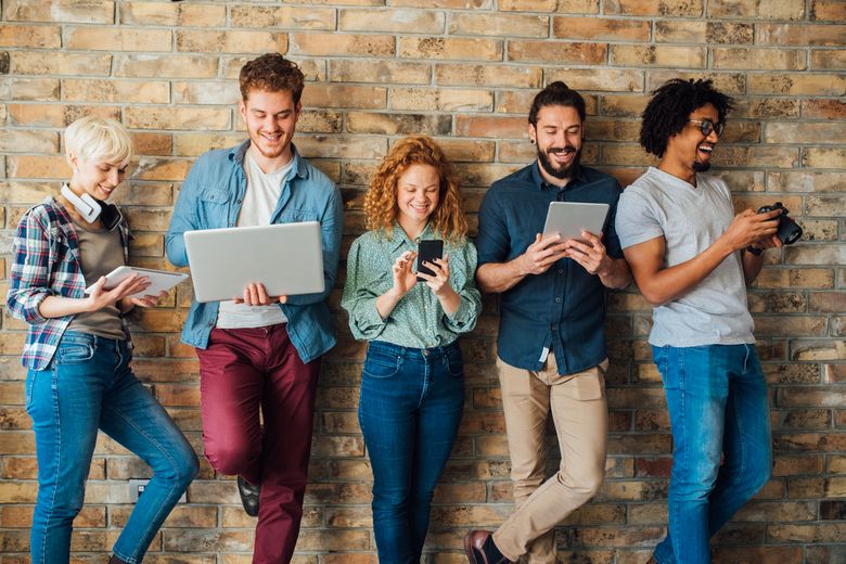 Students using technology and learning Eine Gruppe junge Erwachsene blicken lachend in ihre Tablets und Smartphones. Foto: istock/RgStudio