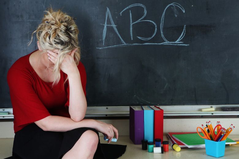 Frustrated elementary teacher Eine Person sitzt vor einer Wandtafel und hat die Stirn in eine Hand gelegt.