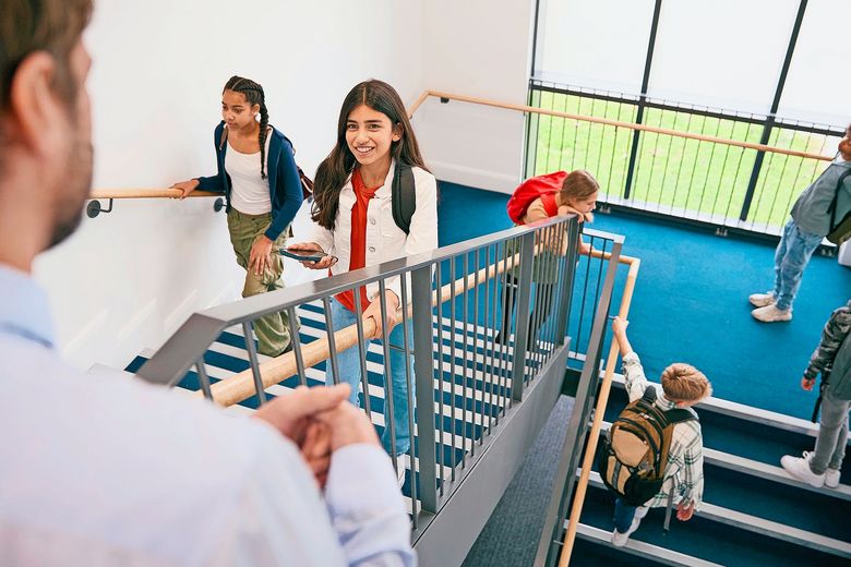 1820293481 Teacher Looking Down On Group Of Secondary Or High School Pupils Inside School Building On Stairs