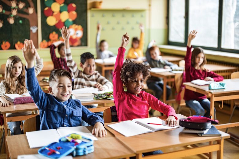 Happy elementary students raising their hands on a class at school. Schulkinder heben im Unterricht ihre Hand.