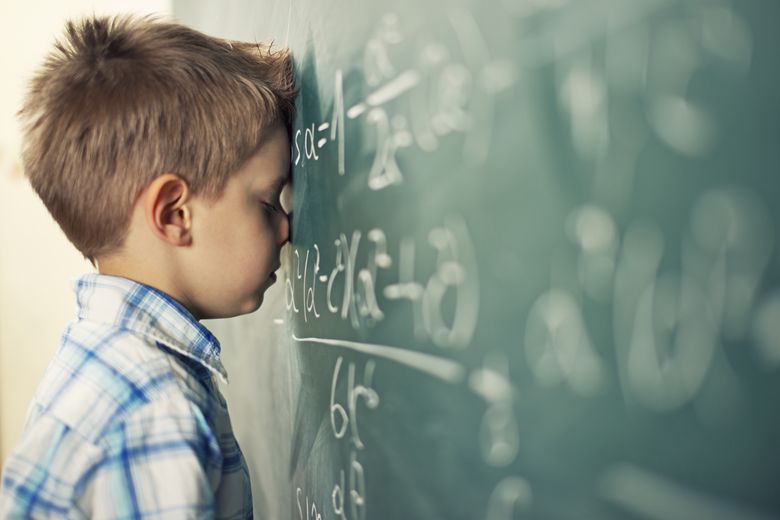 This is too hard Ein Kind lehnt mit der Stirn an eine Wandtafel, auf der mehrere mathematische Formeln stehen.