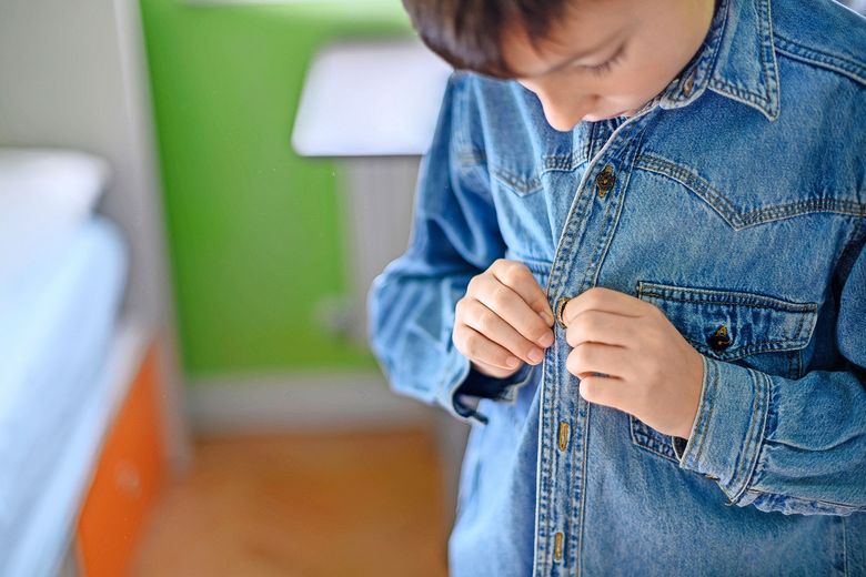 1463514036 Ein Kind knüpft sich das Jeanshemd zu.