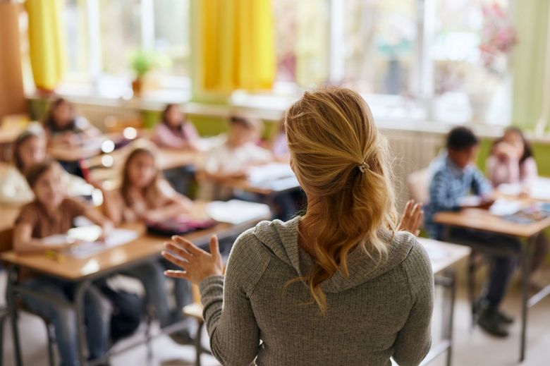 junge Lehrerin steht mit dem Rücken zur Kamera vor einer Schulklasse