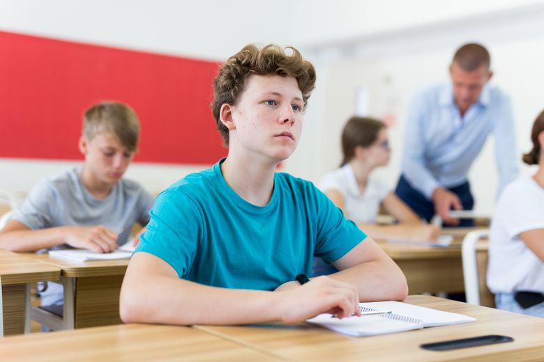 Ein Schüler an einem Pult schaut gedankenverloren vor sich hin.