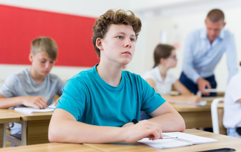 Ein Schüler an einem Pult schaut gedankenverloren vor sich hin.