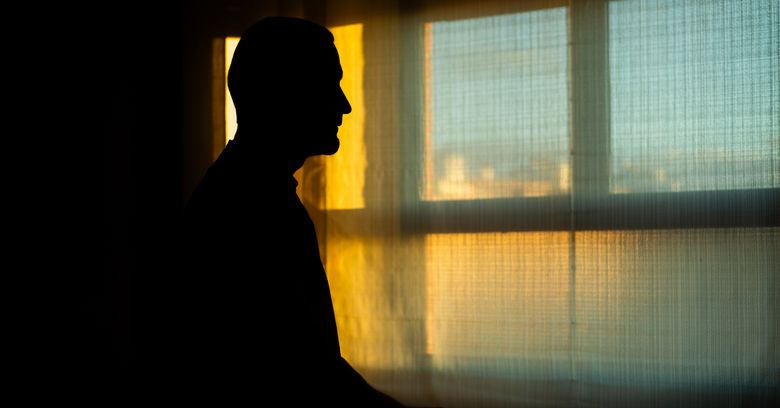 Mann steht im Gegenlicht vor einem Fenster.