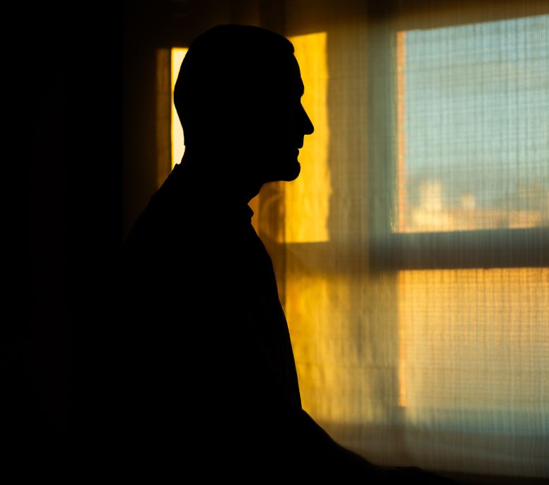 Mann steht im Gegenlicht vor einem Fenster.