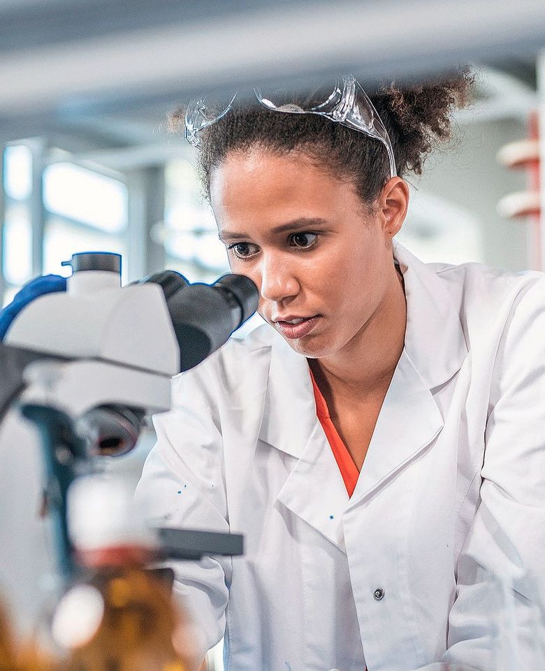 Eine junge Frau schaut in ein Mikroskop.