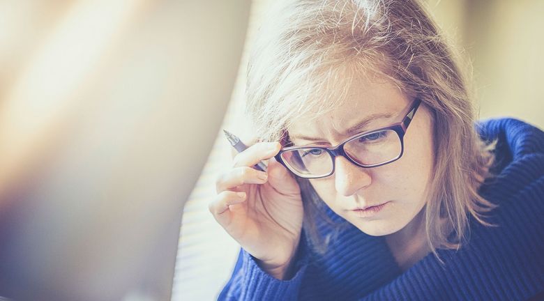 Erwachsene Frau greift sich beim Lesen an die Brille.