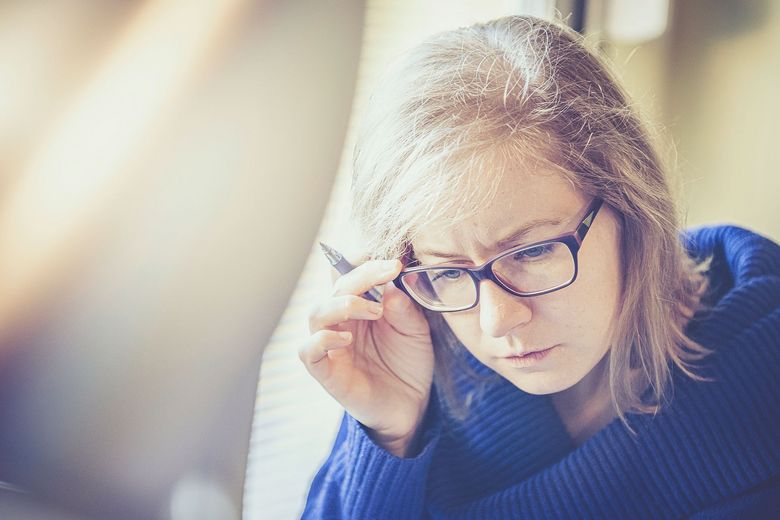 Erwachsene Frau greift sich beim Lesen an die Brille.