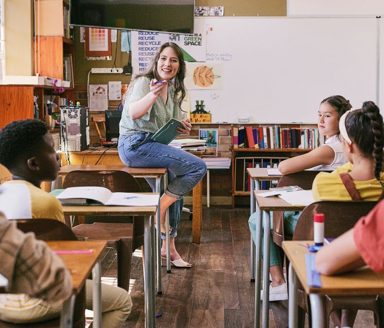 Eine Lehrerin sitzt vor ihrer Klasse auf einem Pult.