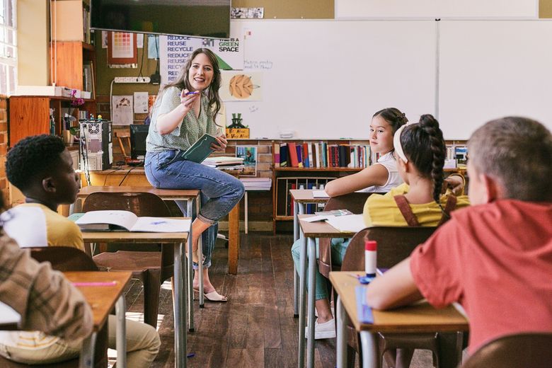 Eine Lehrerin sitzt vor ihrer Klasse auf einem Pult.