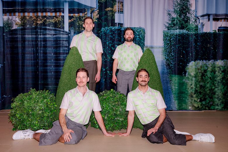 Drei Männer in grauen Hosen und grünweiskarierten Poloshirts stehen auf einer Bühne.